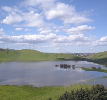 Laguna Seca wetland full of water surrounded by green hillsides under a blue sky