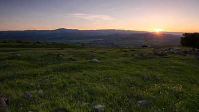 Grassy field with sun rising over distant mountains