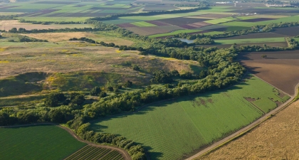 Patchwork of agricultural fields with tree-lined river curving through landscape