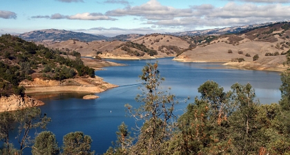 Blue Anderson Reservoir surrounded by brown hills and trees under a blue sky