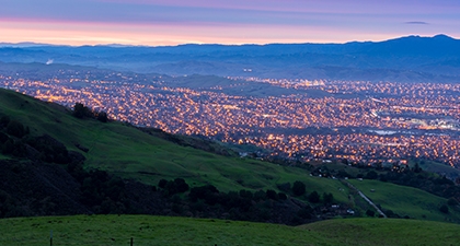 View from green hills of San Jose's city lights below, under a twilight sky