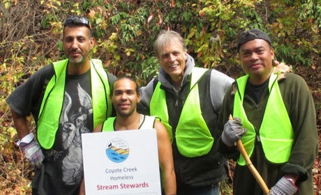 Four men in neon green vests holding sign that says Coyote Creek Homeless Stream Stewards