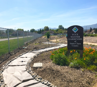 Path leading around garden and wooden sign with UC Master Gardeners of Santa Clara County name and logo