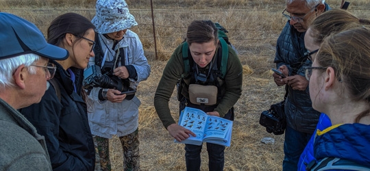 Woman holding bird identification book open to group of hikers around her