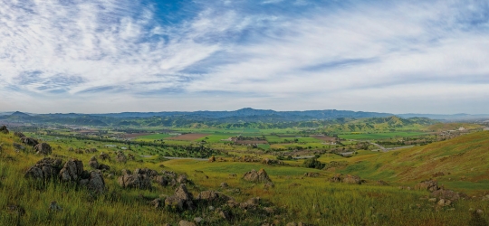 Wide view of green Coyote Valley landscape under blue and white sky, looking west to the Santa Cruz Mountains in the distance